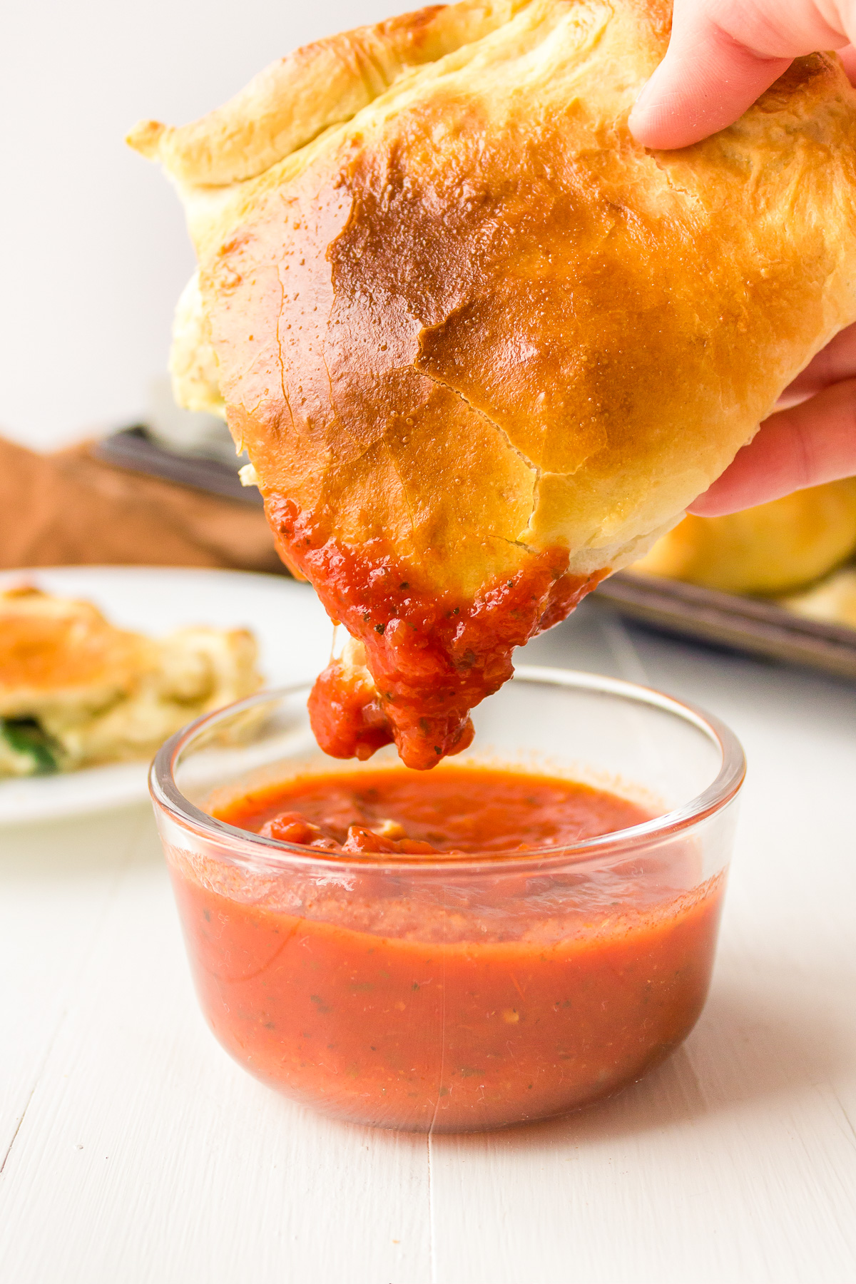 A person's hand dipping a chicken calzone into a bowl of marinara sauce.