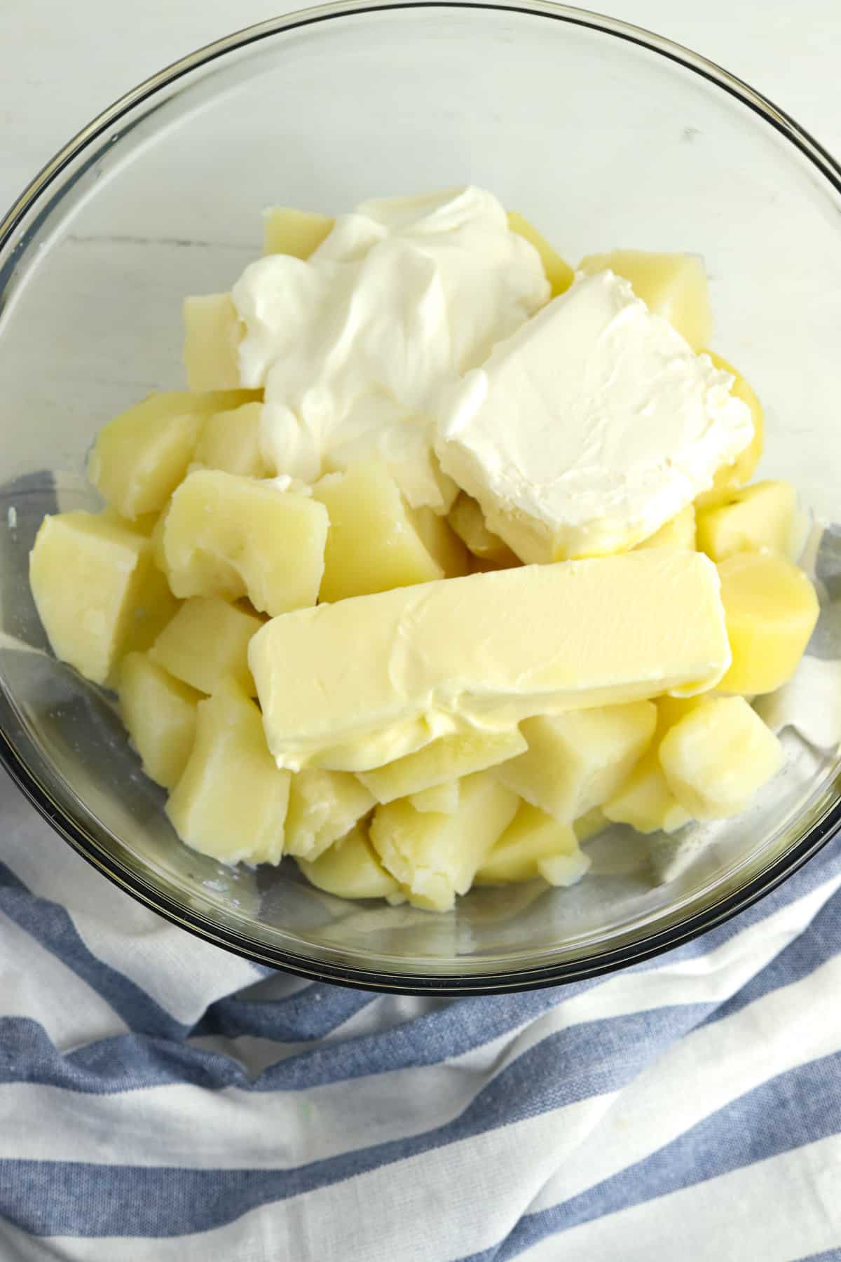 A mixing bowl filled with cooked potatoes, butter, and sour cream and cream cheese