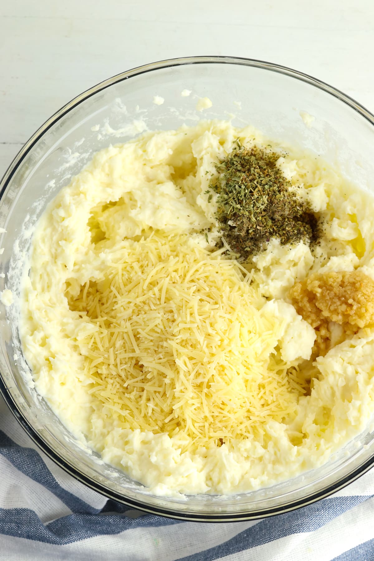 A large mixing bowl of mashed potatoes with cheese and herbs in it