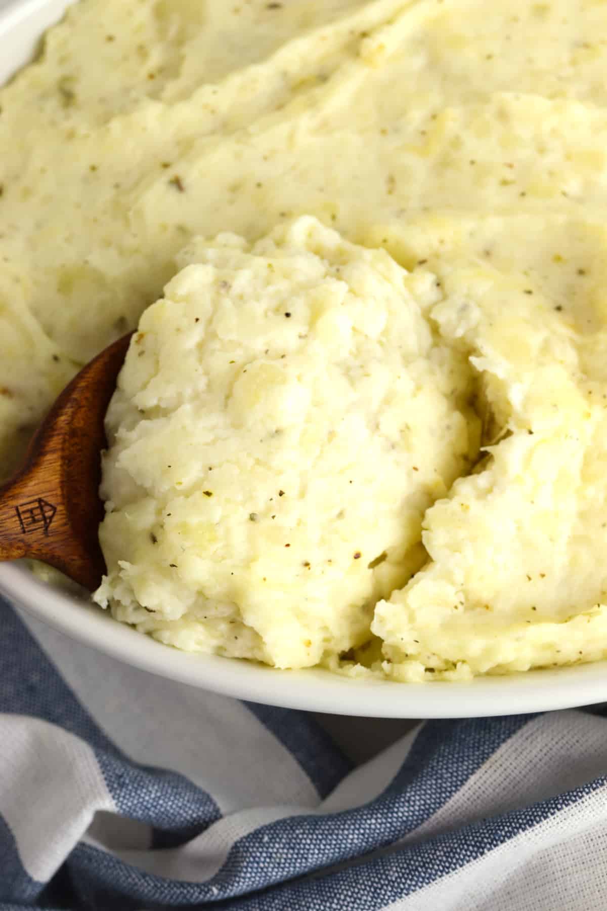 Garlic cream cheese mashed potatoes in a white casserole dish being scooped with a wooden spoon.