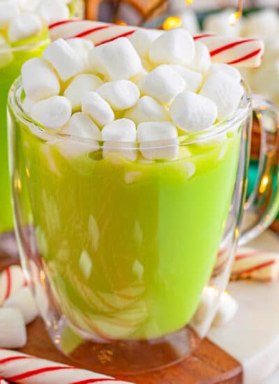 Square up close view of a cup of green hot chocolate with mini marshmallows and a peppermint stick on top.
