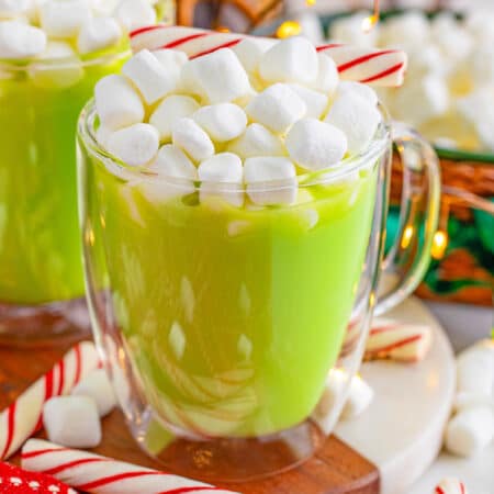 Square up close view of a cup of green hot chocolate with mini marshmallows and a peppermint stick on top.