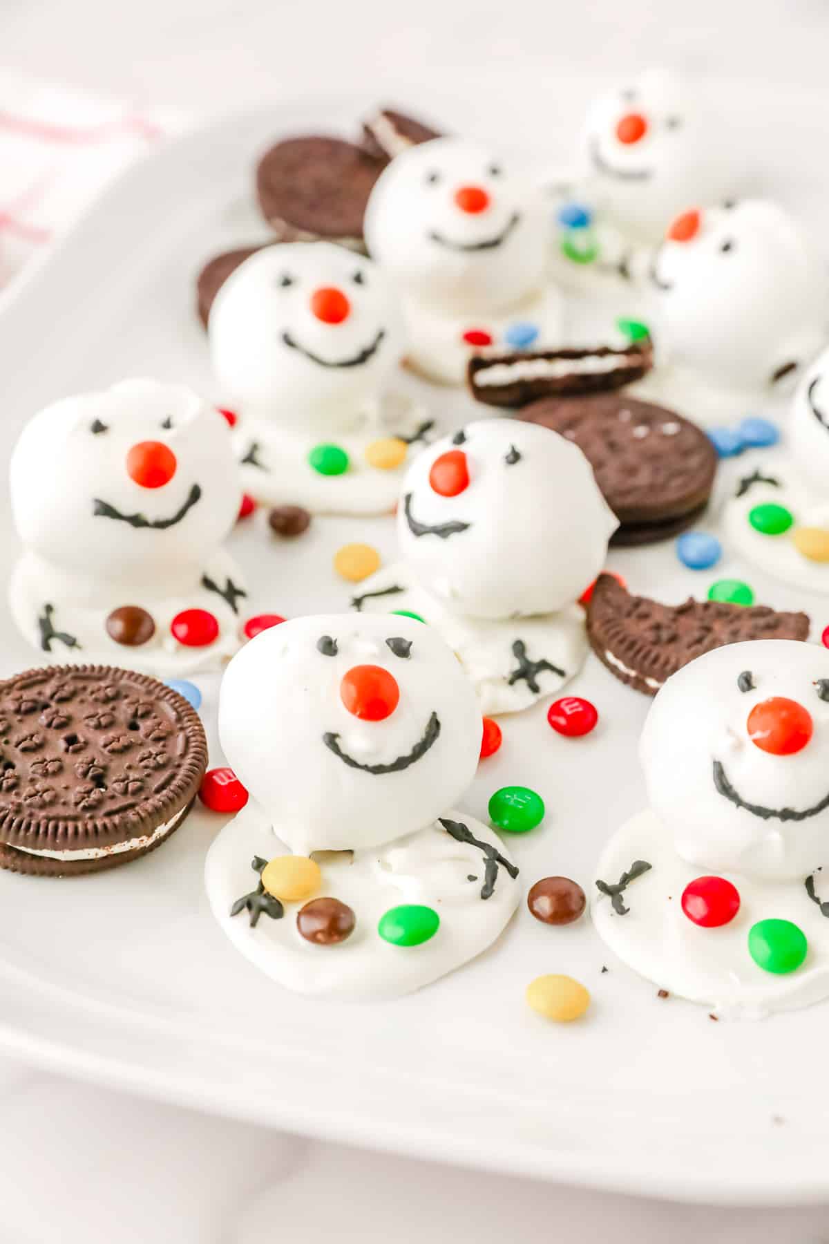 Snowman oreo balls on a platter with more oreo cookies and mini M&Ms.