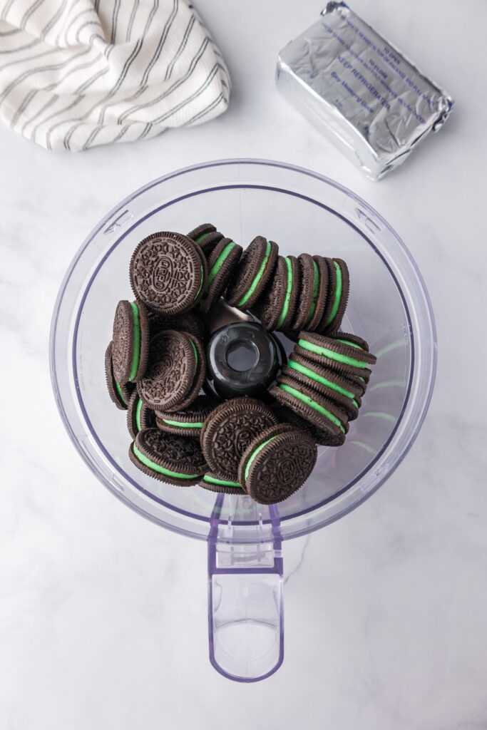 Mint Oreo cookies in a food processor bowl on a marble countertop from above.
