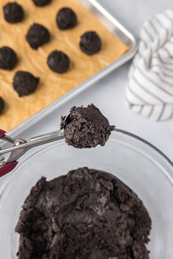 A metal scoop scooping a piece of Oreo mint chocolate truffle dough from a bowl.