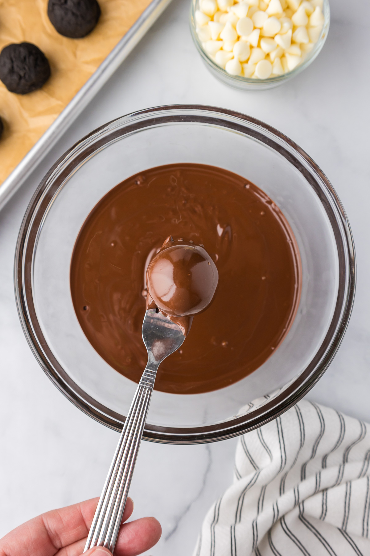 A person dipping a Oreo Mint Chocolate Truffle into a bowl of melted chocolate with a fork.