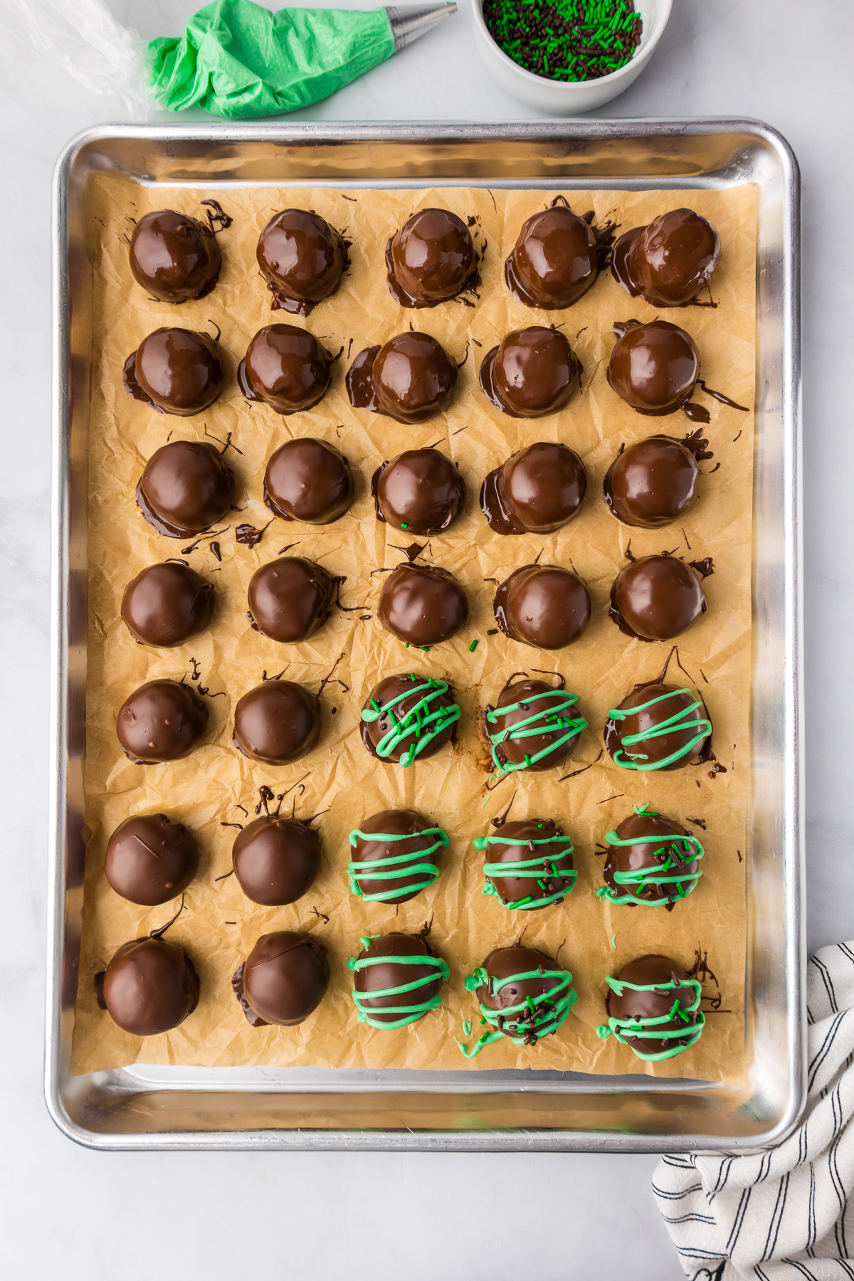 Mint chocolate truffles coated in chocolate on a baking sheet with green chocolate drizzled on top of some truffles.
