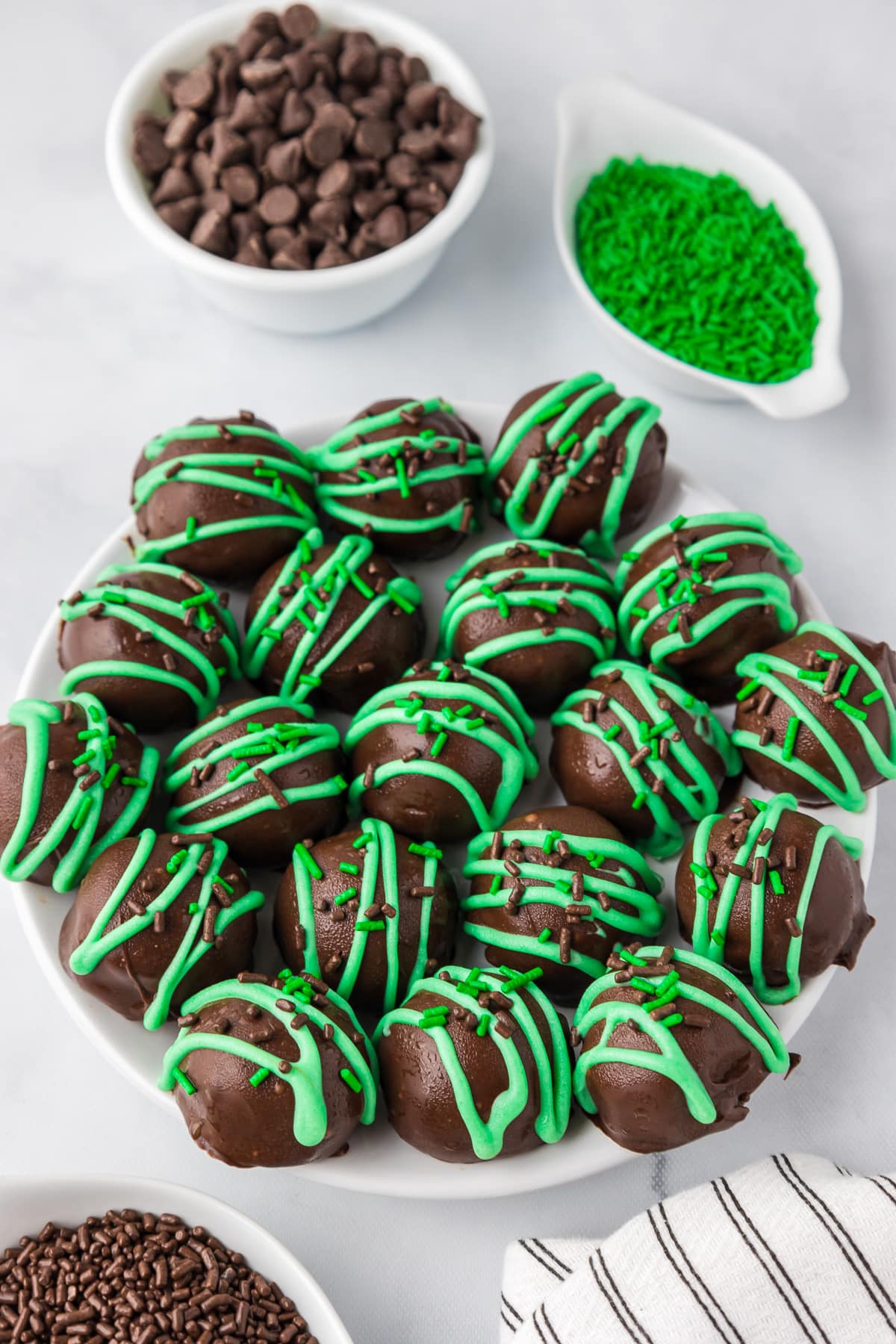 Mint chocolate truffles piled on a plate from overhead with green drizzled chocolate and sprinkles.