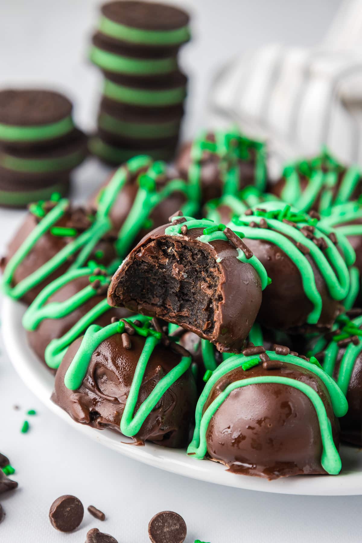 Mint oreo truffles with green drizzled chocolate piled on a plate with one missing a bite.