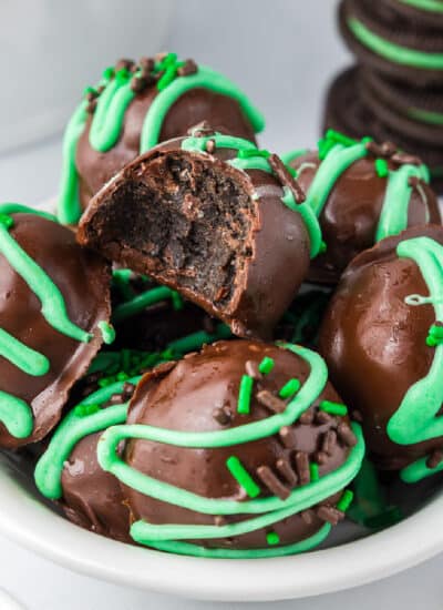 Chocolate oreo truffles in a white bowl with green sprinkles with the top piece missing a bite.
