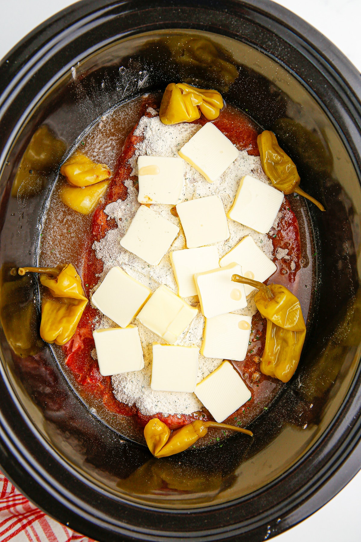 A crock pot filled with chuck roast beef, butter, seasoning and pepperoncini peppers.