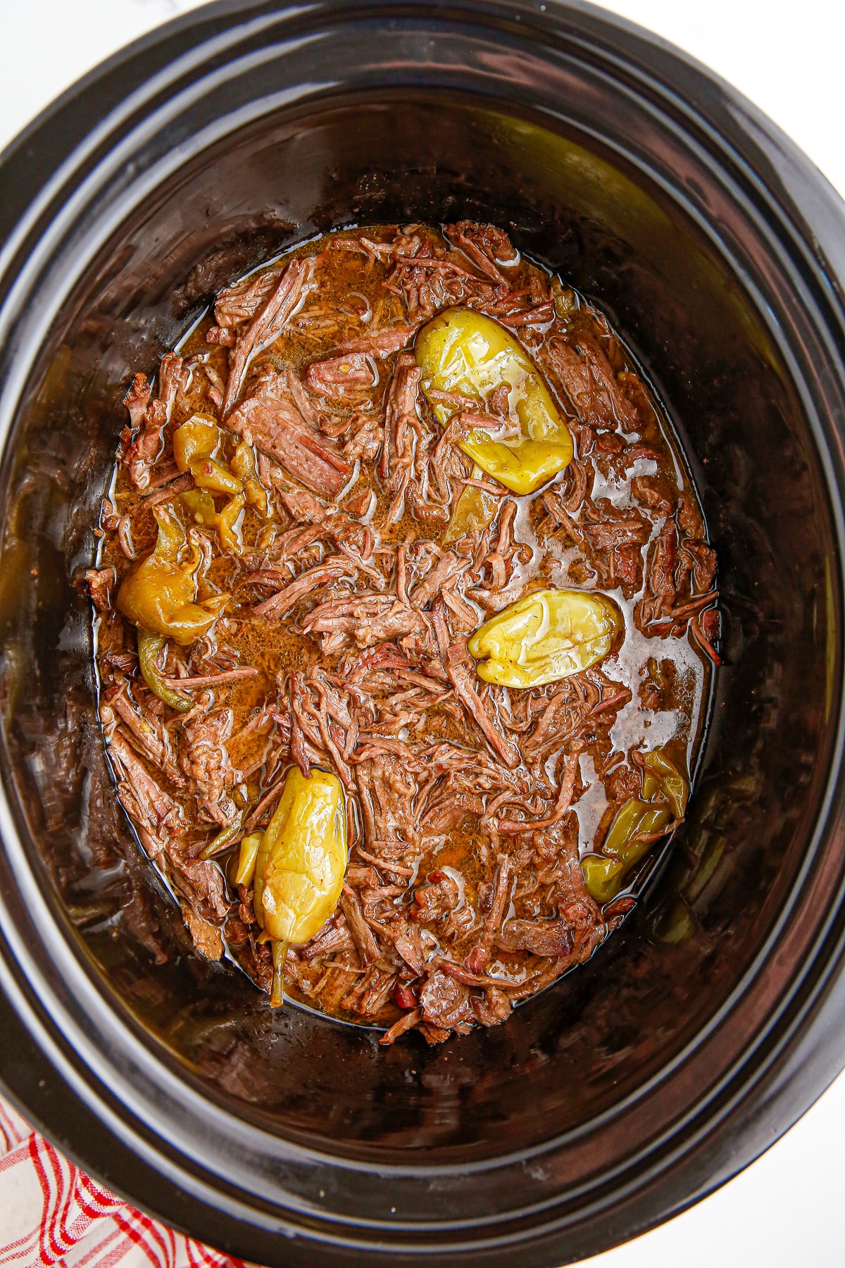 A crock pot filled with shredded Mississippi pot roast beef and peppers.
