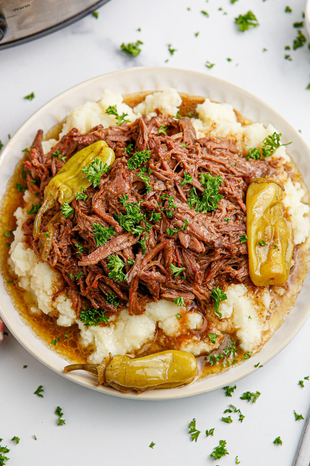 A plate with shredded mississippi pot roast on top of mashed potatoes with pepperoncini peppers on top from above.