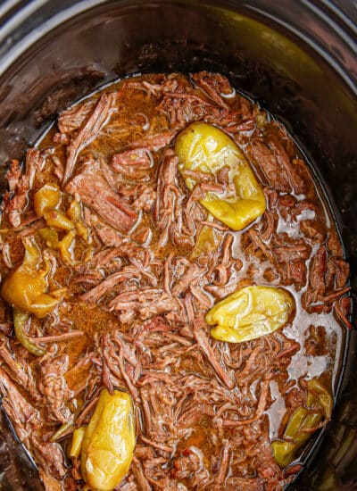 A slow cooker filled with shredded Mississippi pot roast beef, cooking liquid and peppers from above.