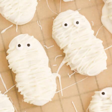 Mummy Nutter Butter cookies with white chocolate decorations cooling on parchment paper.