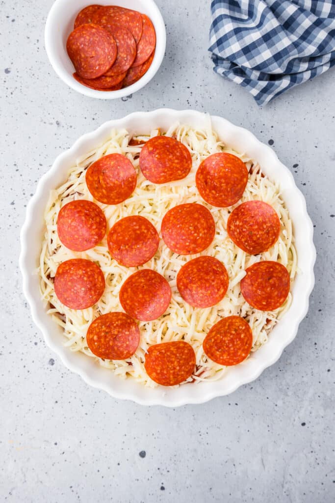 Pepperoni dip in a white round dish covered in pepperonis before baking.