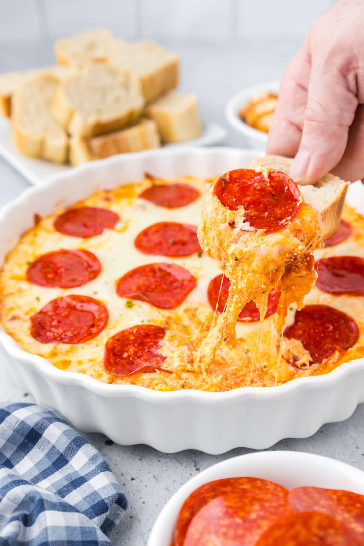 A person dipping a slice of bread into pepperoni dip in a round dish.