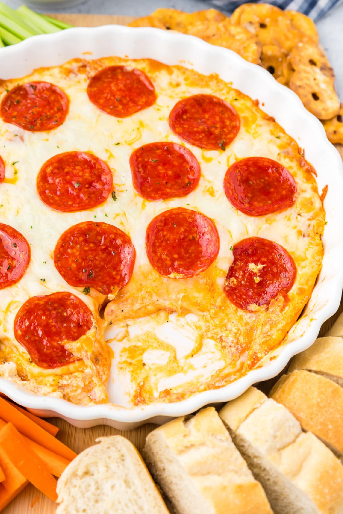 Pepperoni dip in a white dish with a scoop missing and carrots, celery, bread and pretzel chips around the dip on a platter.