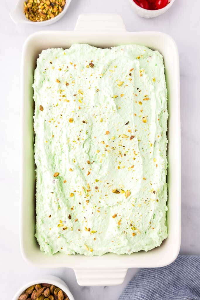 Pistachio cake in a rectangular baking dish frosted with green frosting and topped with chopped pistachios.