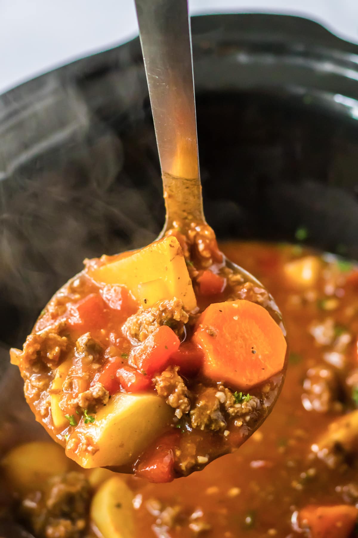 A ladle with a scoop of poor man's stew is being held over a slow cooker full of stew.