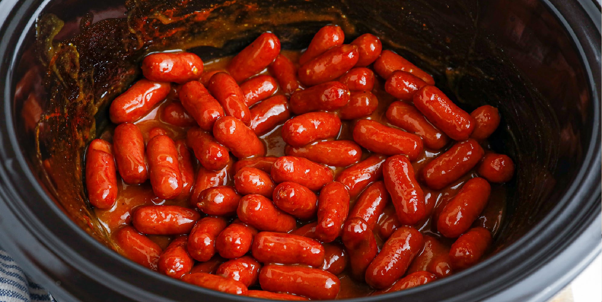 Wide view of saucy bbq little smokies in a slow cooker base.