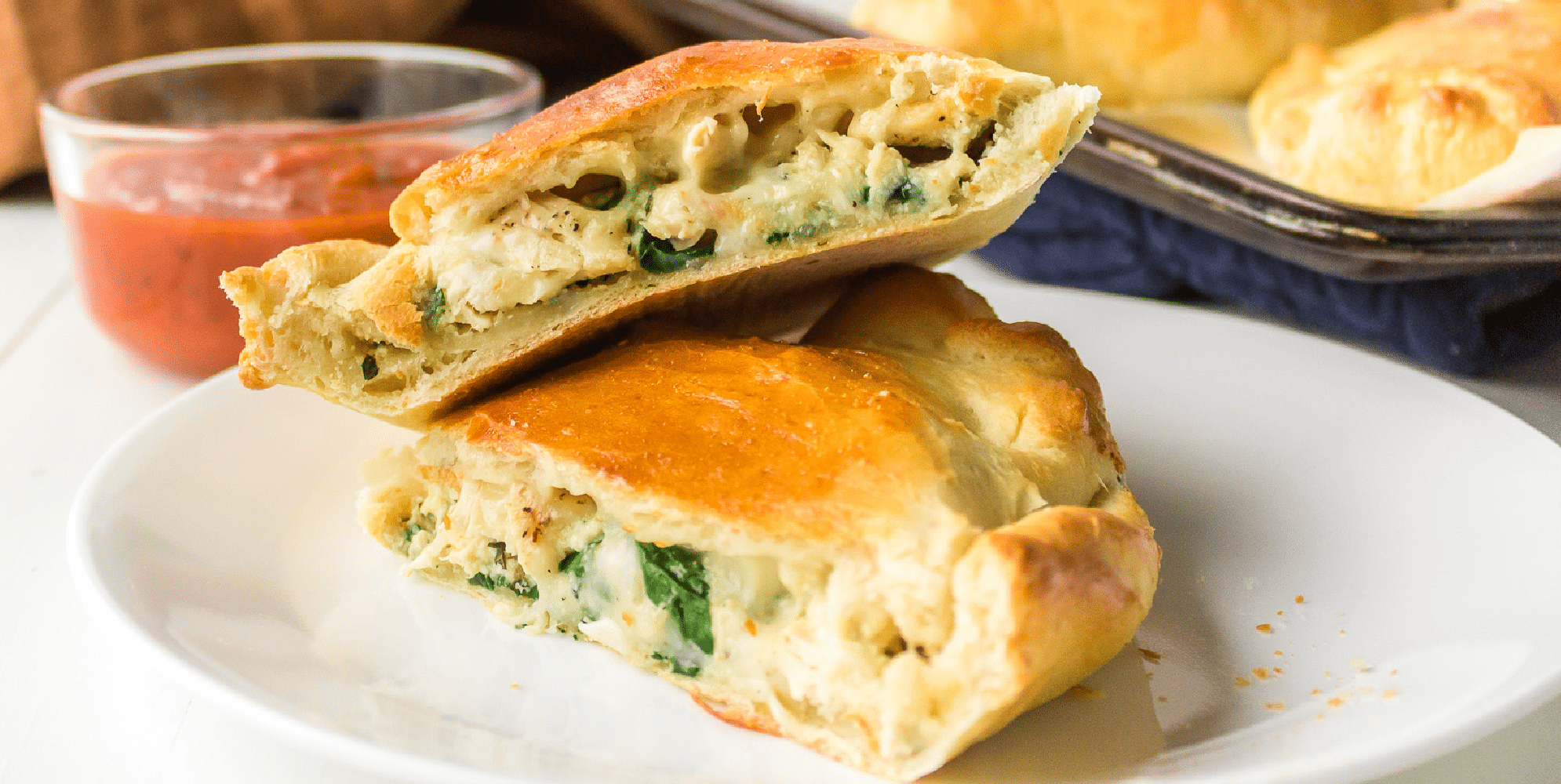 Wide view of chicken, cheese and spinach calzones cut in half to see the filling stacked on a plate.