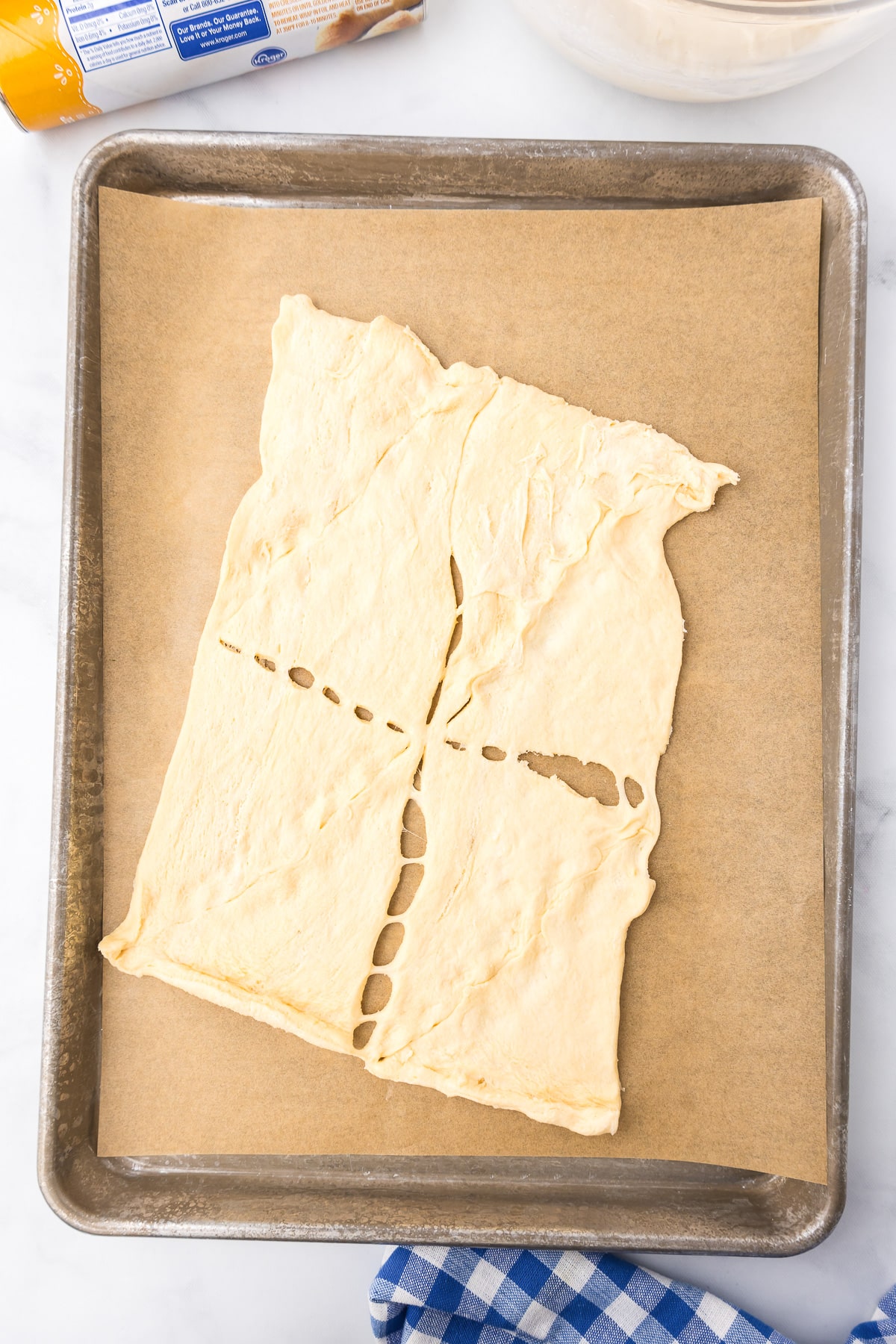 A sheet of crescent roll dough spread out on a parchment paper lined baking sheet, with some of the dough seams pressed together.