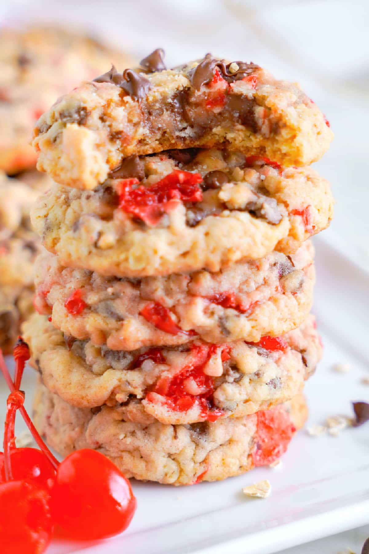 A stack of maraschino cherry cookies chocolate chip cookies with the top cookie missing a bite.