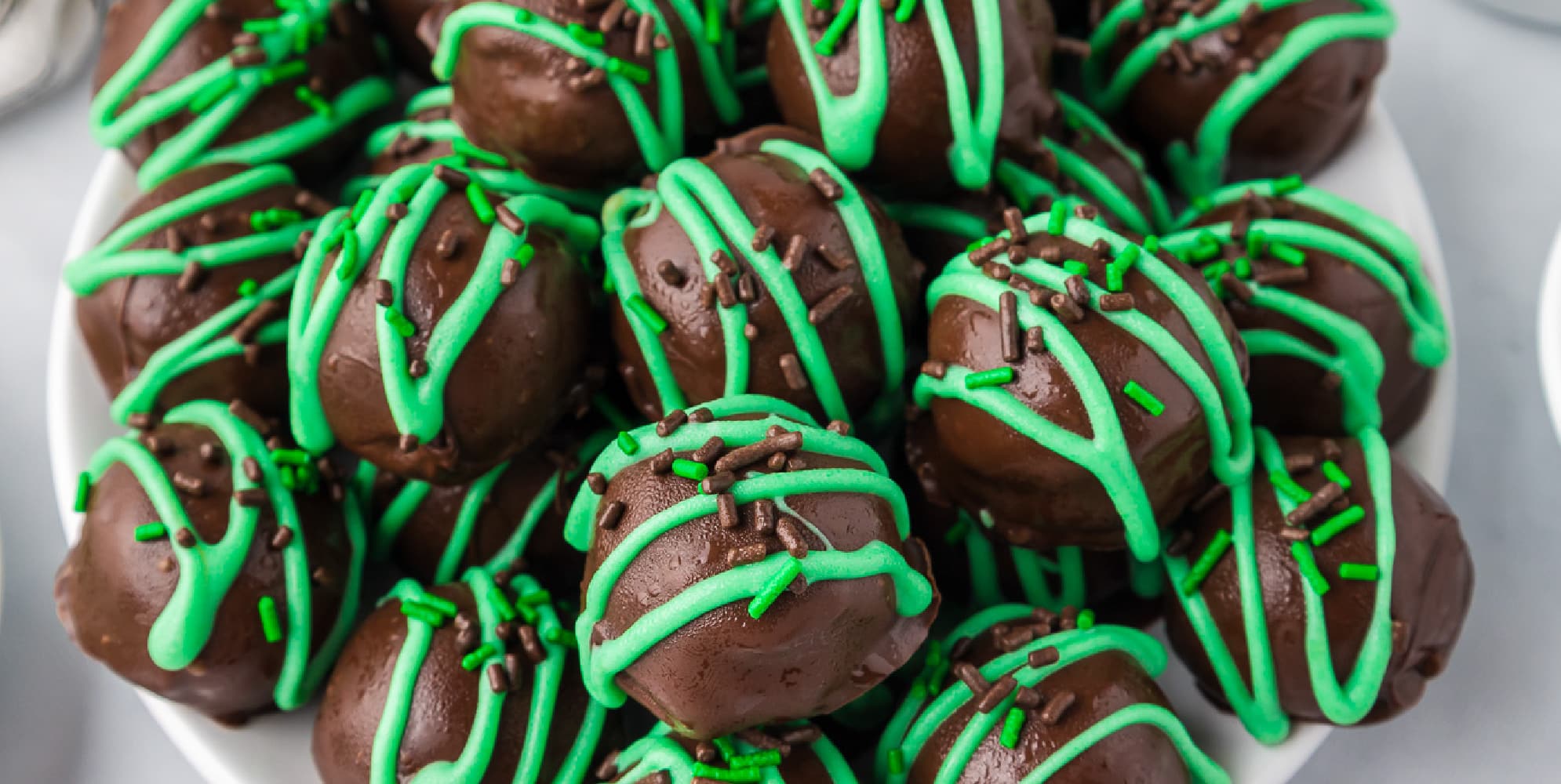 Mint Oreo truffles stacked on a platter with green drizzled chocolate and sprinkles.