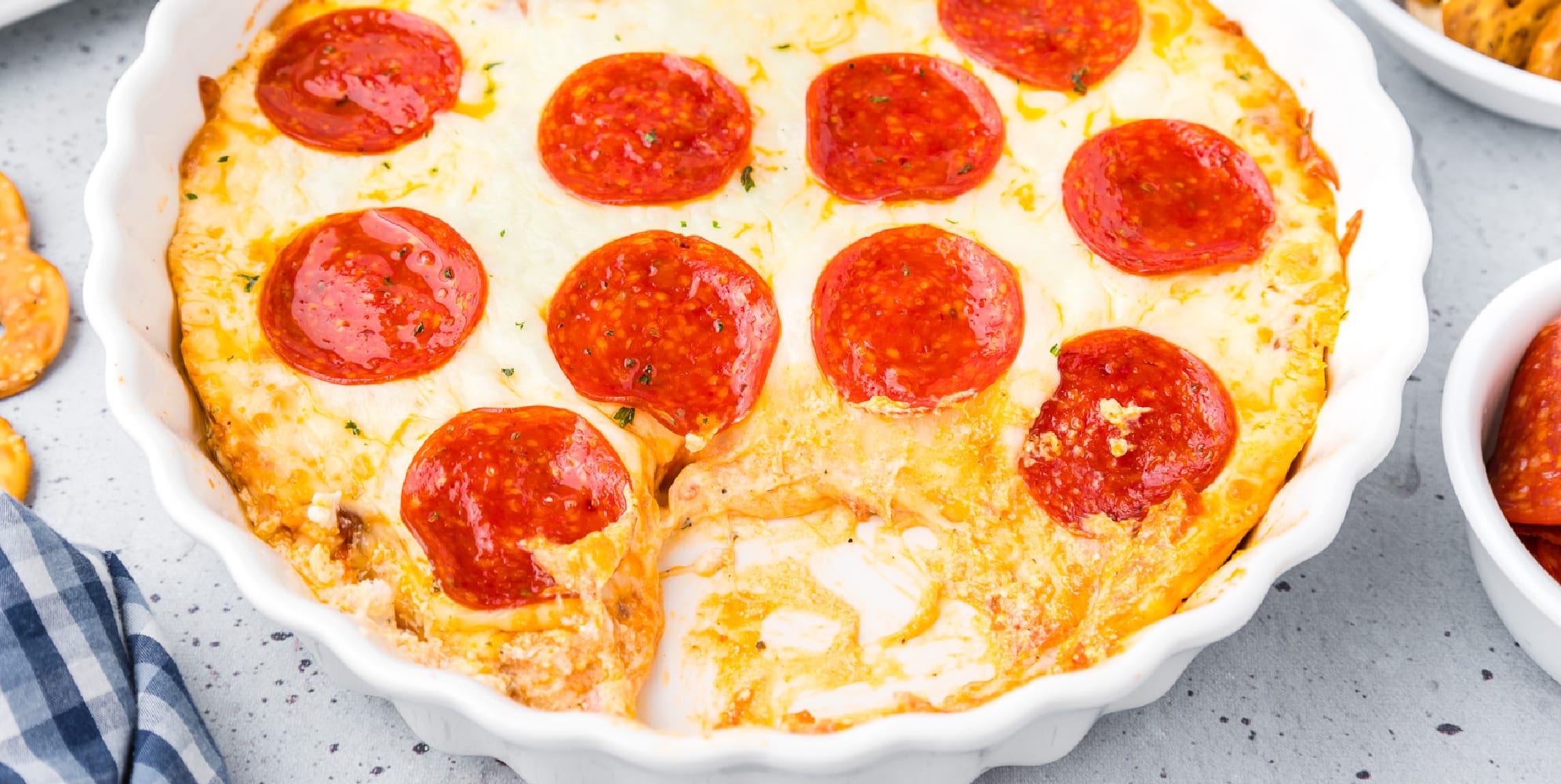 Wide view of pepperoni dip in a white dish missing a scoop.