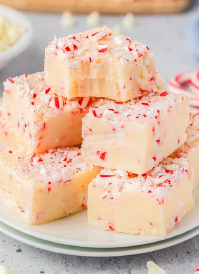 Peppermint fudge piled high on a plate topped with pieces of candy cane with the top piece missing a bite.