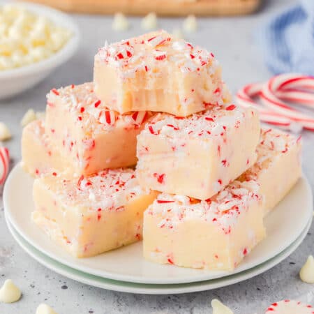 Peppermint fudge piled high on a plate topped with pieces of candy cane with the top piece missing a bite.