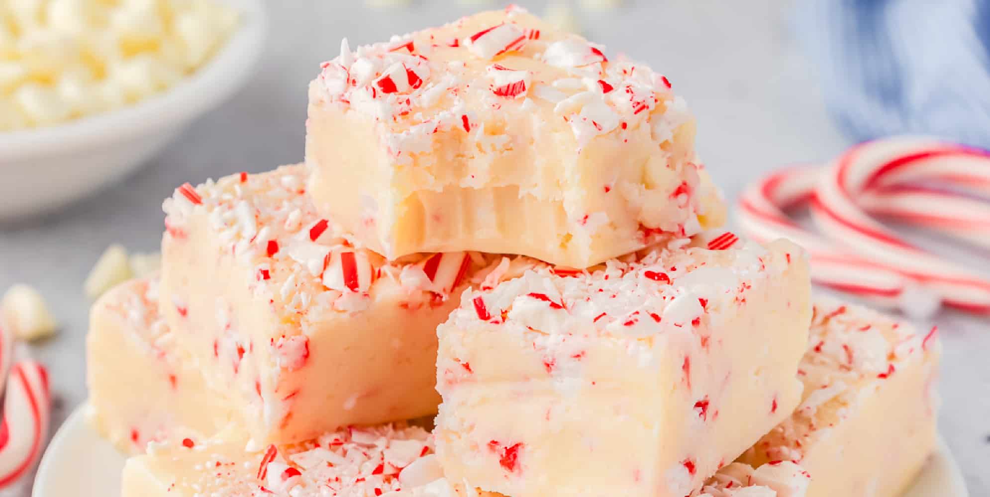 A stack of peppermint fudge topped with candy cane pieces close up with the top piece missing a bite.