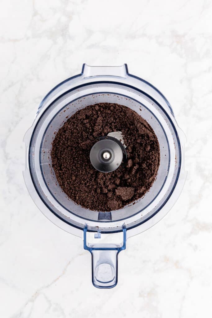 A food processor with chocolate Oreo cookie crumbs inside from above.