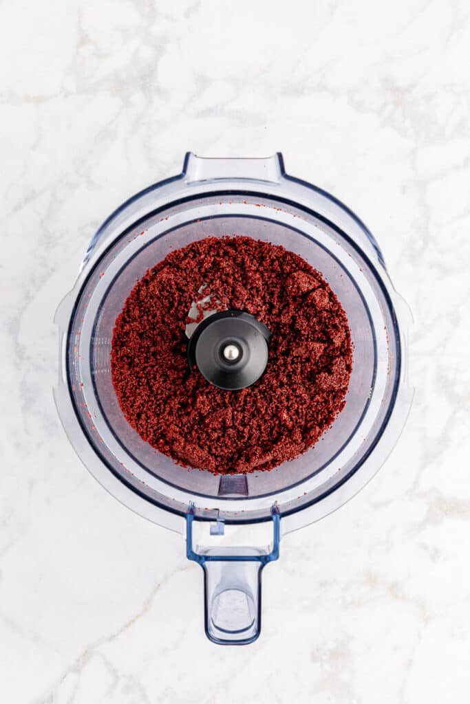 A food processor with red velvet Oreo cookie crumbs inside from above.