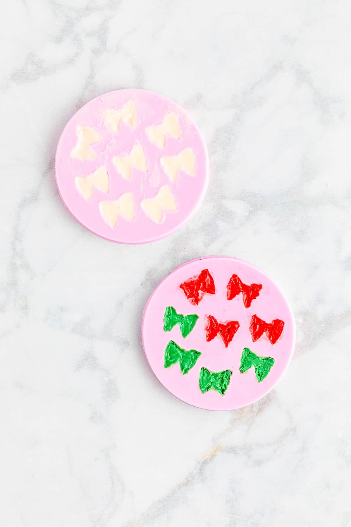 two pink silicone molds with bow shapes full of white, red and green chocolate.
