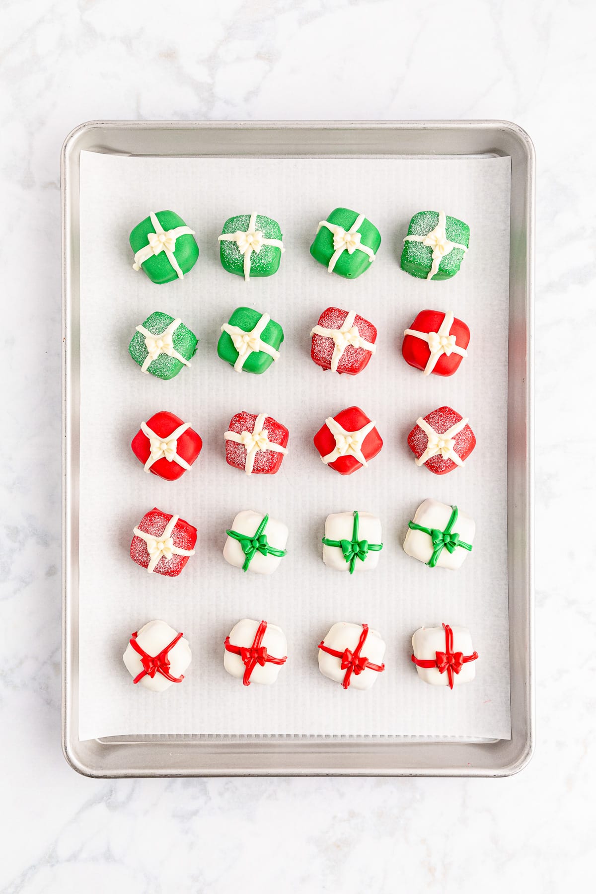Christmas present chocolate truffles on a baking sheet with red, green, and white ribbon stripes after decorating.