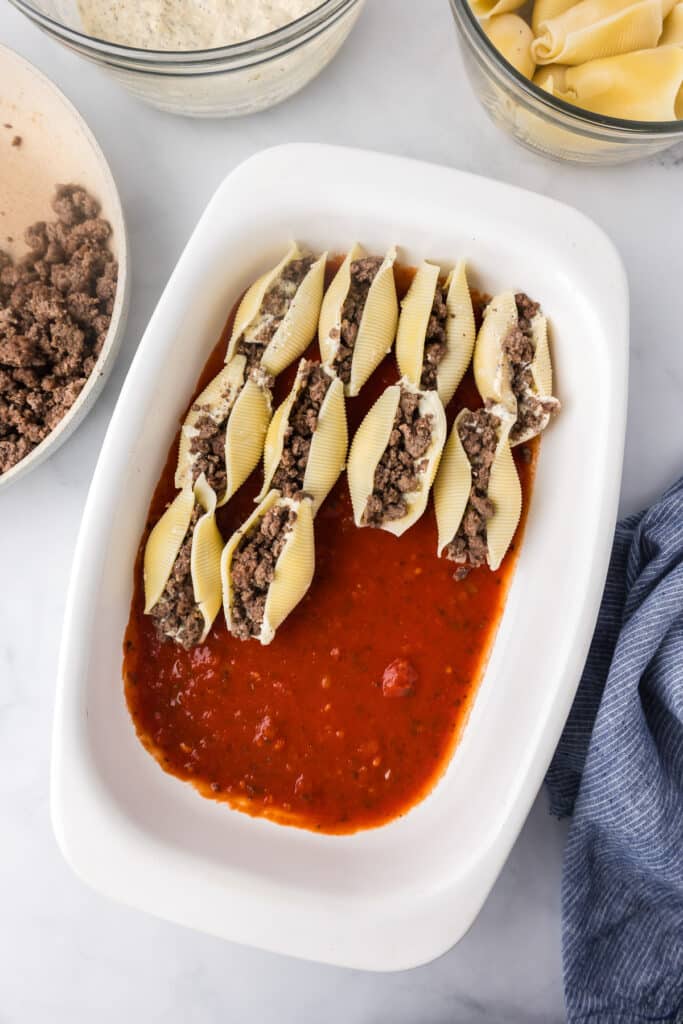Stuffed shell pasta full of beef and cheese in a white dish with marinara sauce.