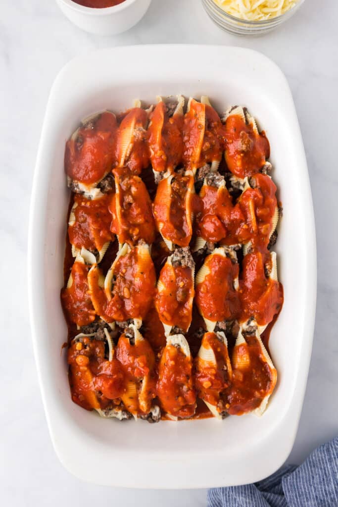 Beef stuffed shells covered in marinara sauce unbaked in a white baking dish from above.