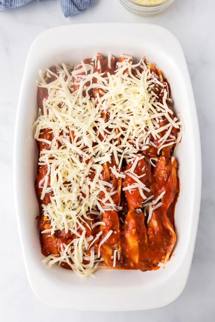 Beef stuffed shells covered in marinara sauce and half covered in cheese unbaked in a white baking dish from above.