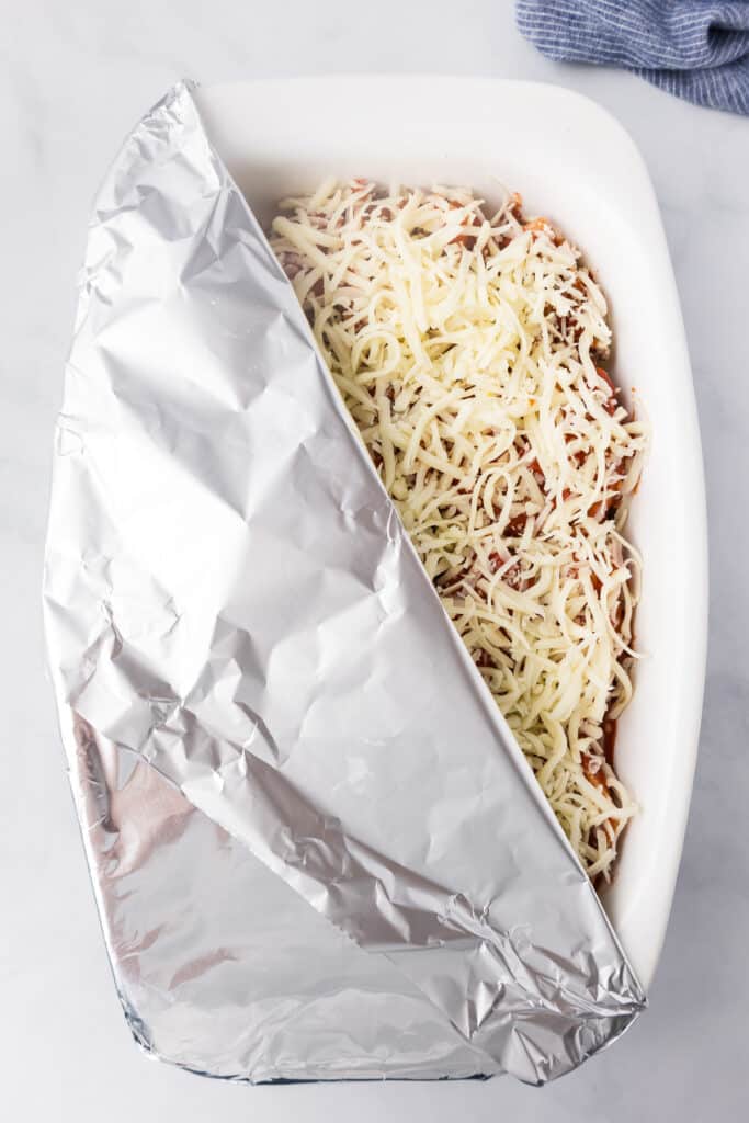 A casserole dish covered in foil with cheese on top of beef stuffed shells from above.