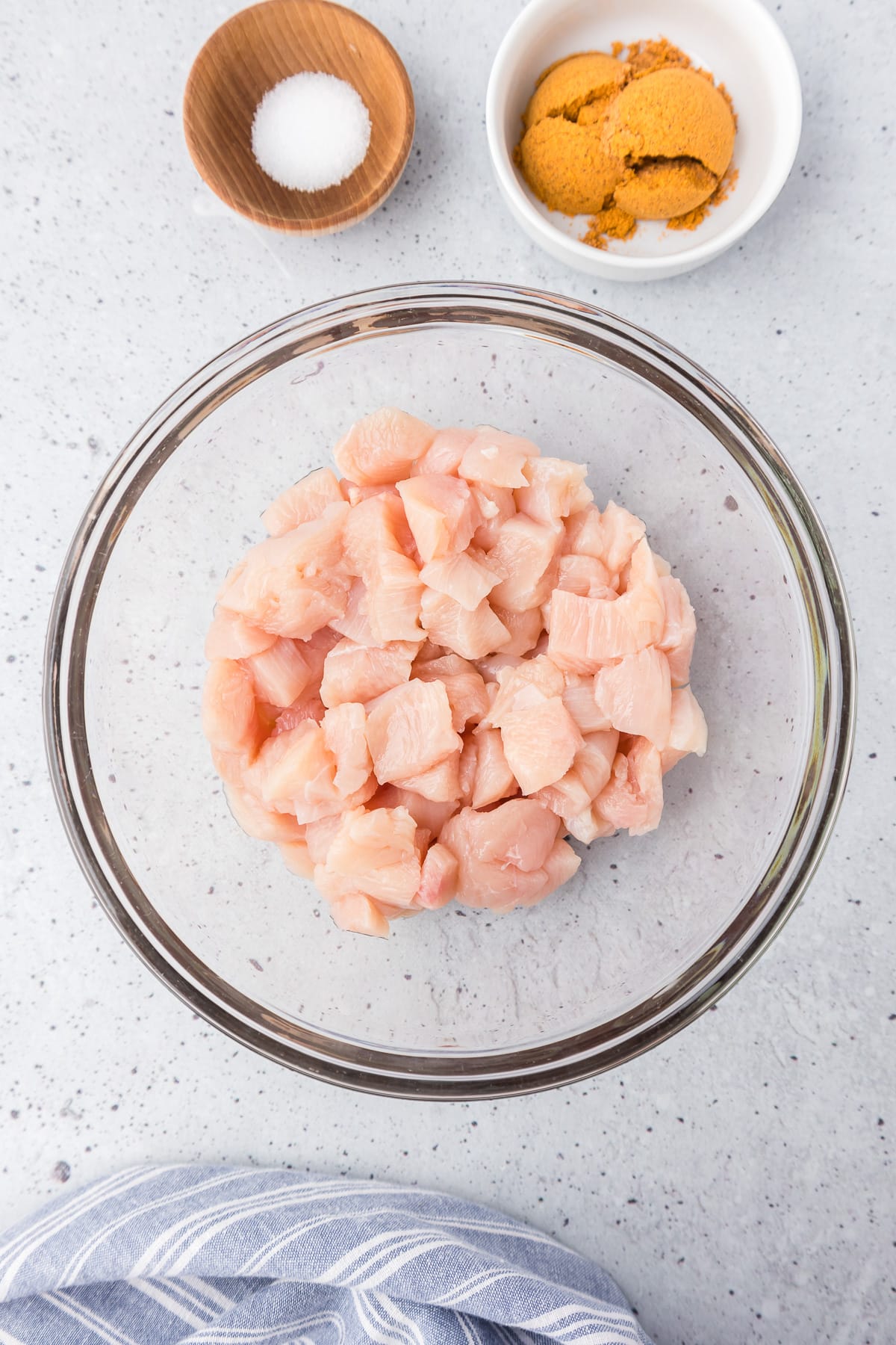 Diced raw chicken breast in a large bowl on a counter with salt and taco seasoning in small bowls nearby.