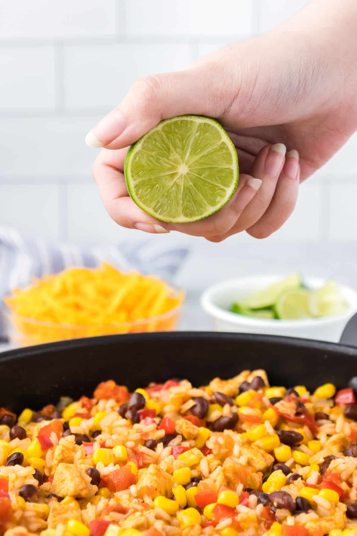 A person holding a lime squeezing it over a pan of Mexican chicken and rice.