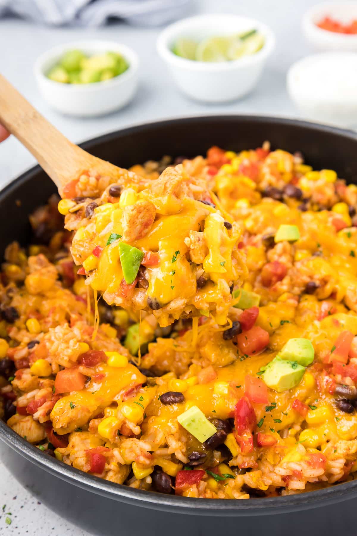 Mexican rice with chicken, vegetables and cheese in a skillet with a wooden spoon lifting a spoonful.