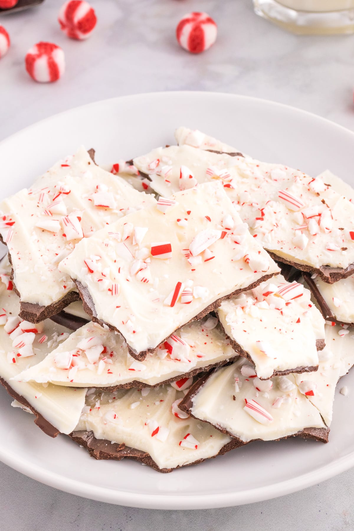 Peppermint bark on a white plate with peppermint candy nearby on the counter.