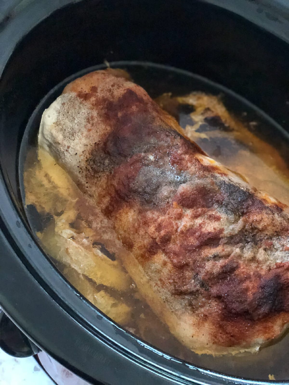 A piece of meat is being cooked in a slow cooker.