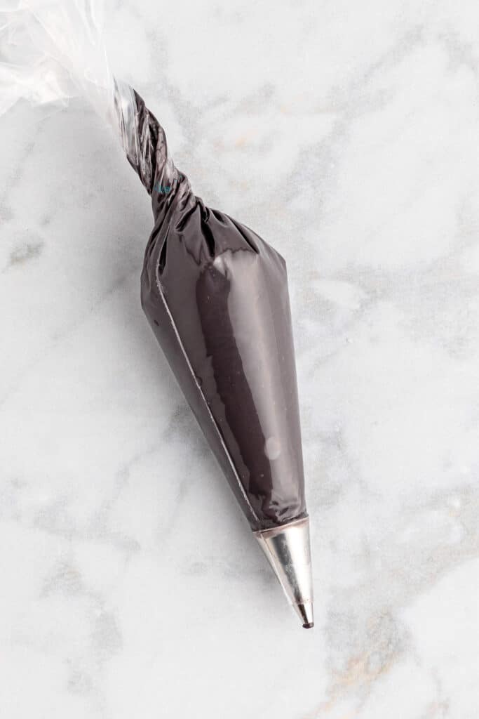 A piping bag fitted with a metal tip full of black melted chocolate.