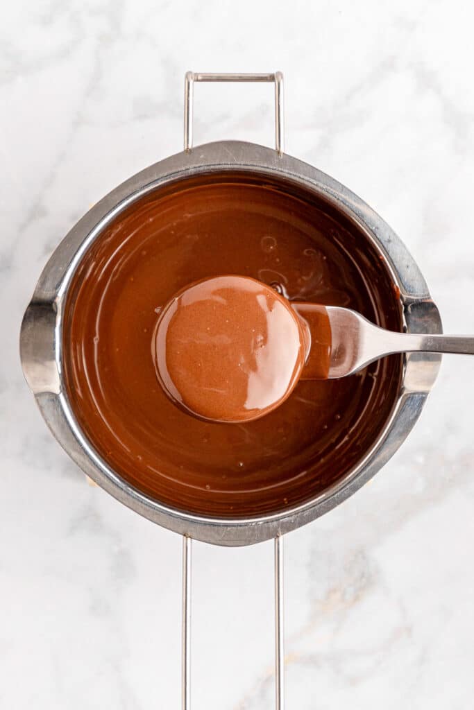 Melted chocolate in a pan with a chocolate dipped Oreo being lifted from the chocolate.