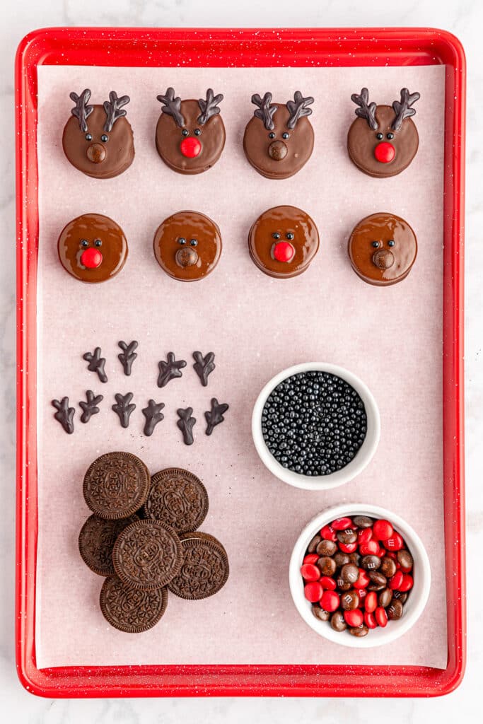 A tray of chocolate reindeer Oreo cookies being decorated on a baking tray.