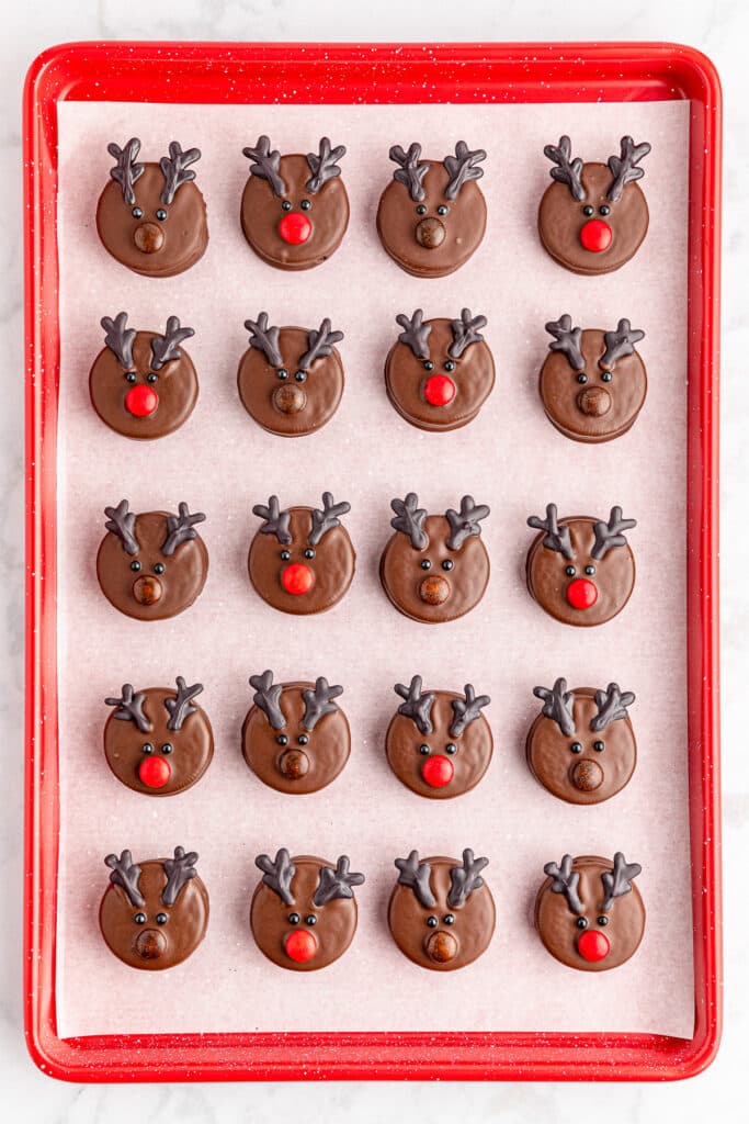 Chocolate decorated reindeer Oreo cookies lined up on a baking tray.